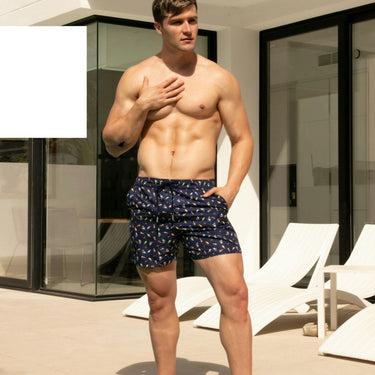 Man standing by a pool wearing navy swim trunks with white patterns.